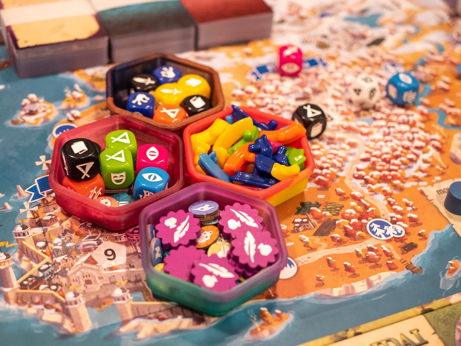 Four hexagonal token holders filled with colourful game pieces, arranged on a game board